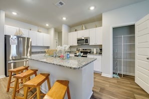 A modern kitchen with a central island, wooden stools, stainless steel appliances, and white cabinetry.