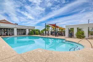 Una piscina con sillas de descanso y sombrillas, rodeada de edificios y palmeras.
