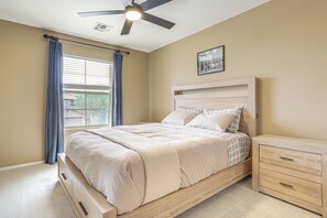 A bedroom with a bed, a nightstand, a ceiling fan, a window with curtains, and a framed picture on the wall.