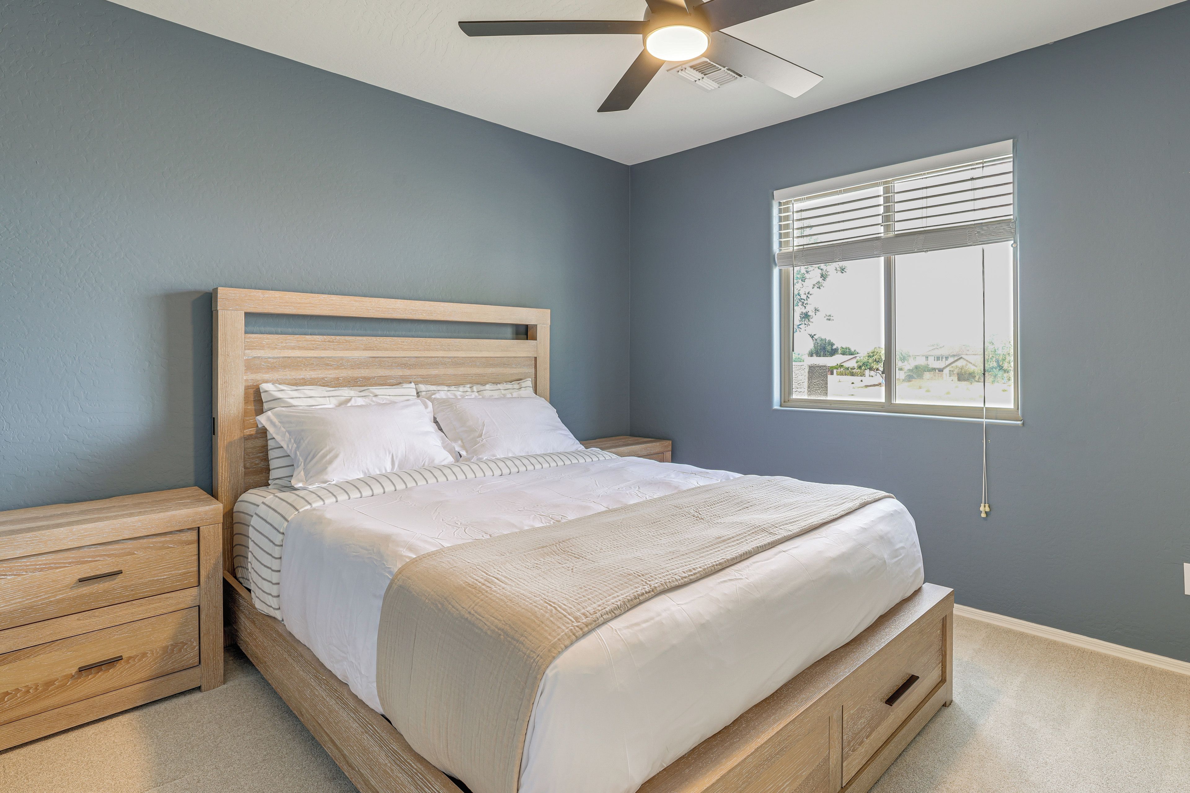 A bedroom with a bed, nightstands, a ceiling fan, and a window with blinds.
