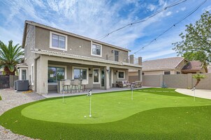 Una casa de dos pisos con un porche cubierto, un césped con campo de práctica de golf y una piscina.