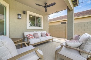 A covered outdoor seating area with a sofa, chairs, and a ceiling fan.
