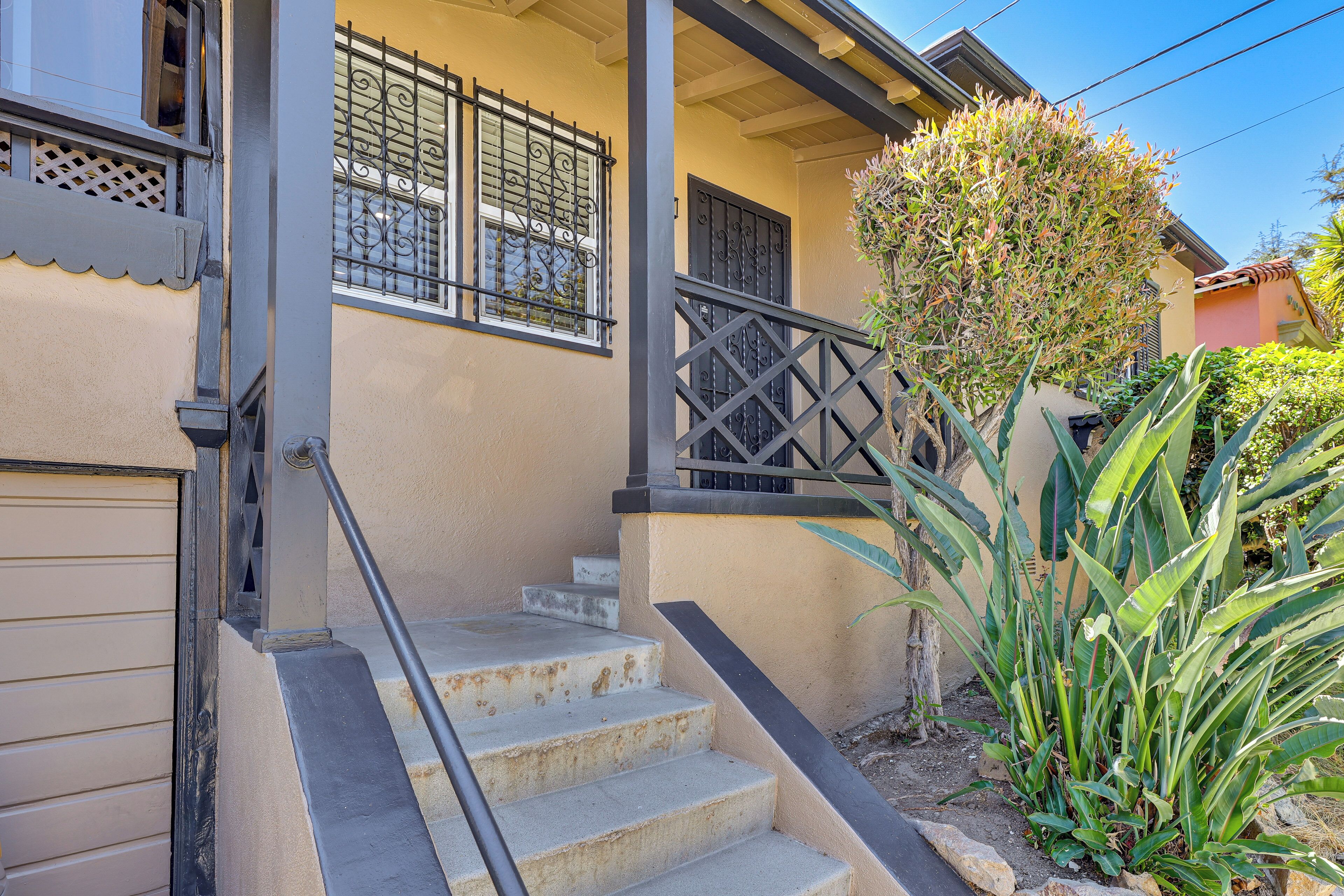 A residential building with a beige exterior, a staircase with a metal railing, and a small garden with tropical plants.