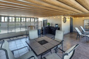 An outdoor patio area with a table and chairs, a small kitchen area, and a seating area with a view.