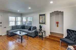 A living room with a sectional sofa, a glass coffee table, a black armchair, and a painting on the wall. - Walk to Metro! Historic View Park Home w/ Patio (Los Angeles)