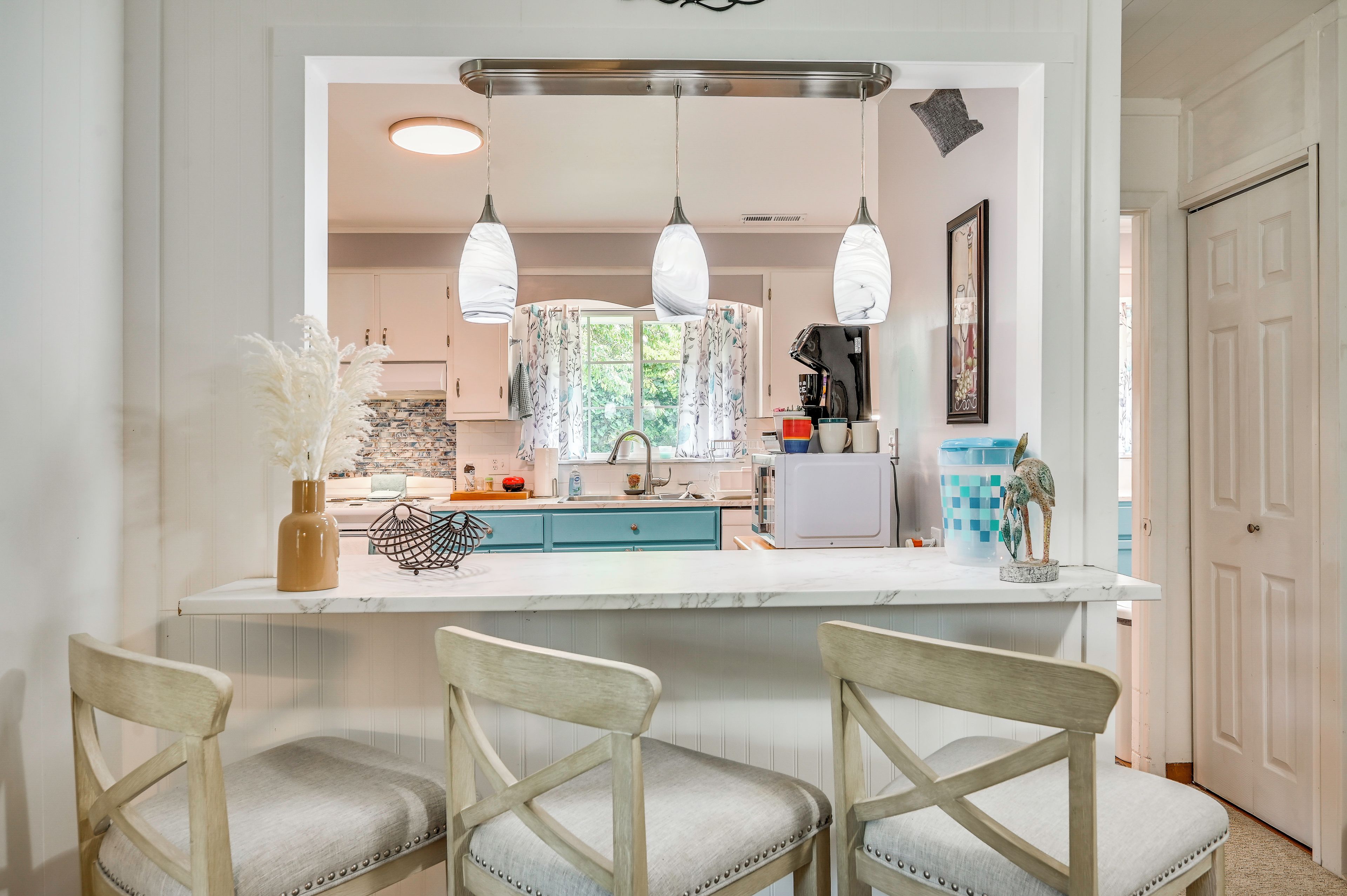 A kitchen with a central island, pendant lights, and a view of the outdoors.