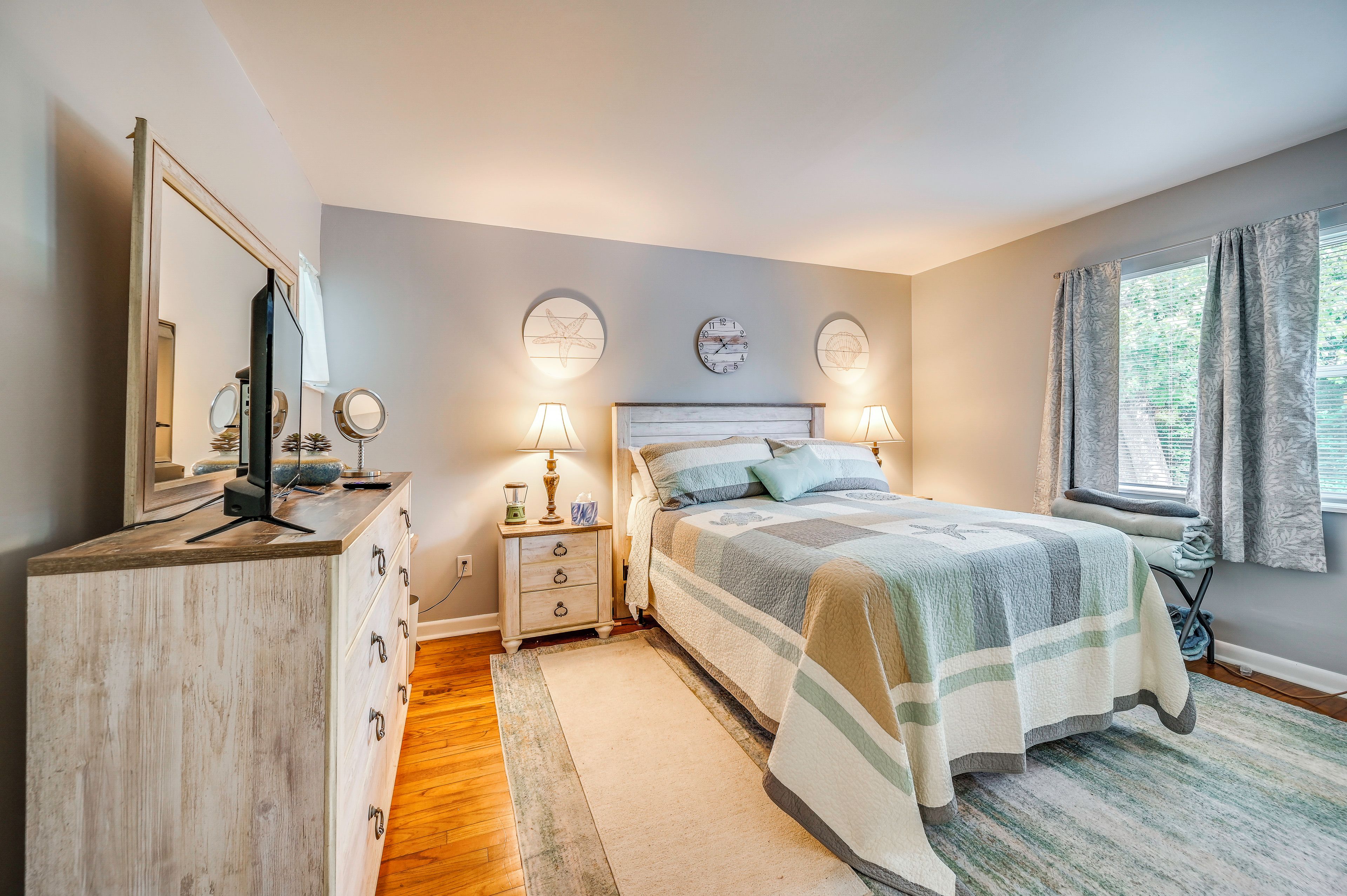 A bedroom with a bed, bedside lamps, a dresser, a mirror, and a window with curtains.