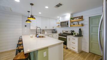 A modern kitchen with white cabinets, a central island, stainless steel appliances, and pendant lighting.