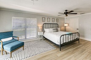 Ein Schlafzimmer mit Bett, Stuhl, Nachttisch, Stehlampe und Deckenventilator.
