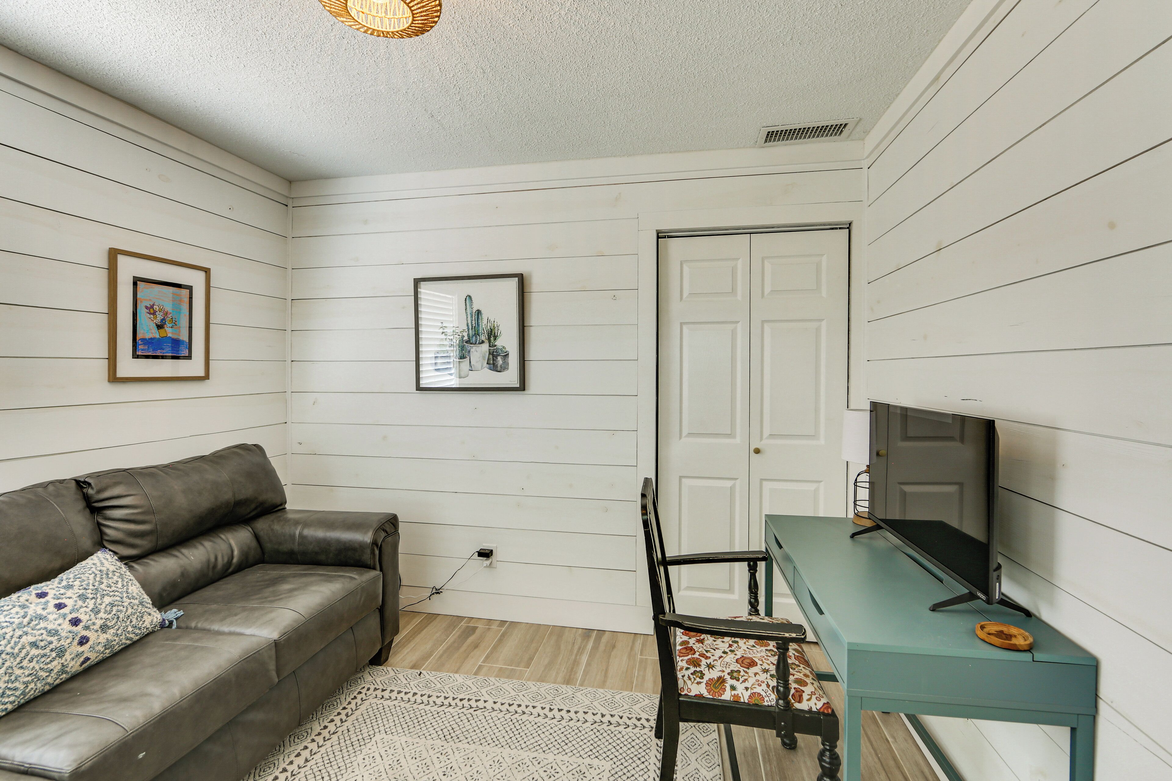 A room with a sofa, a desk with a computer, a chair, and two framed pictures on the wall.