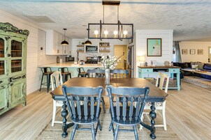 A dining area with a wooden table and chairs, a kitchen in the background, and a living room with a sofa and a TV.