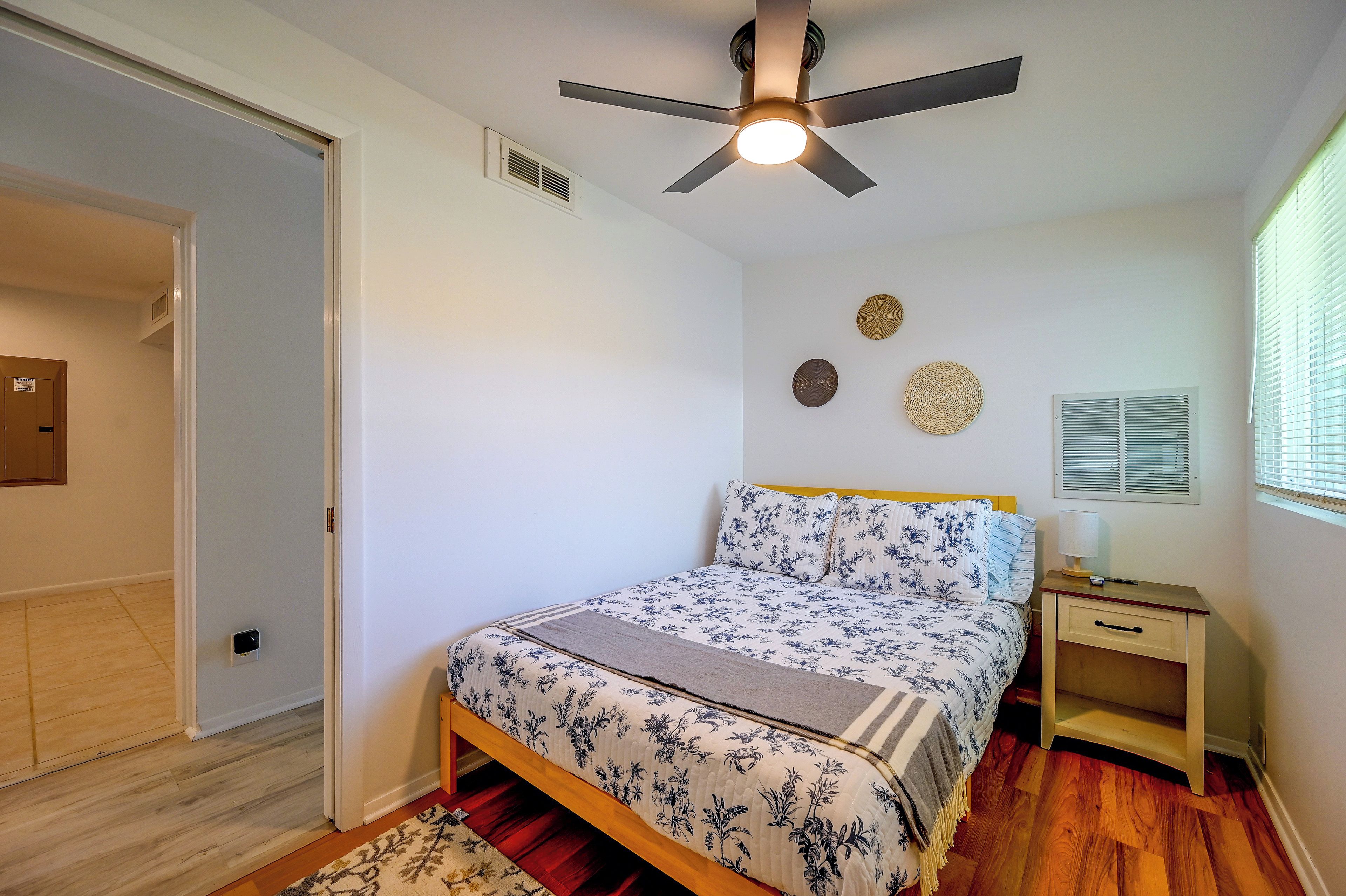 A bedroom with a bed, a nightstand, a ceiling fan, and a window with blinds.