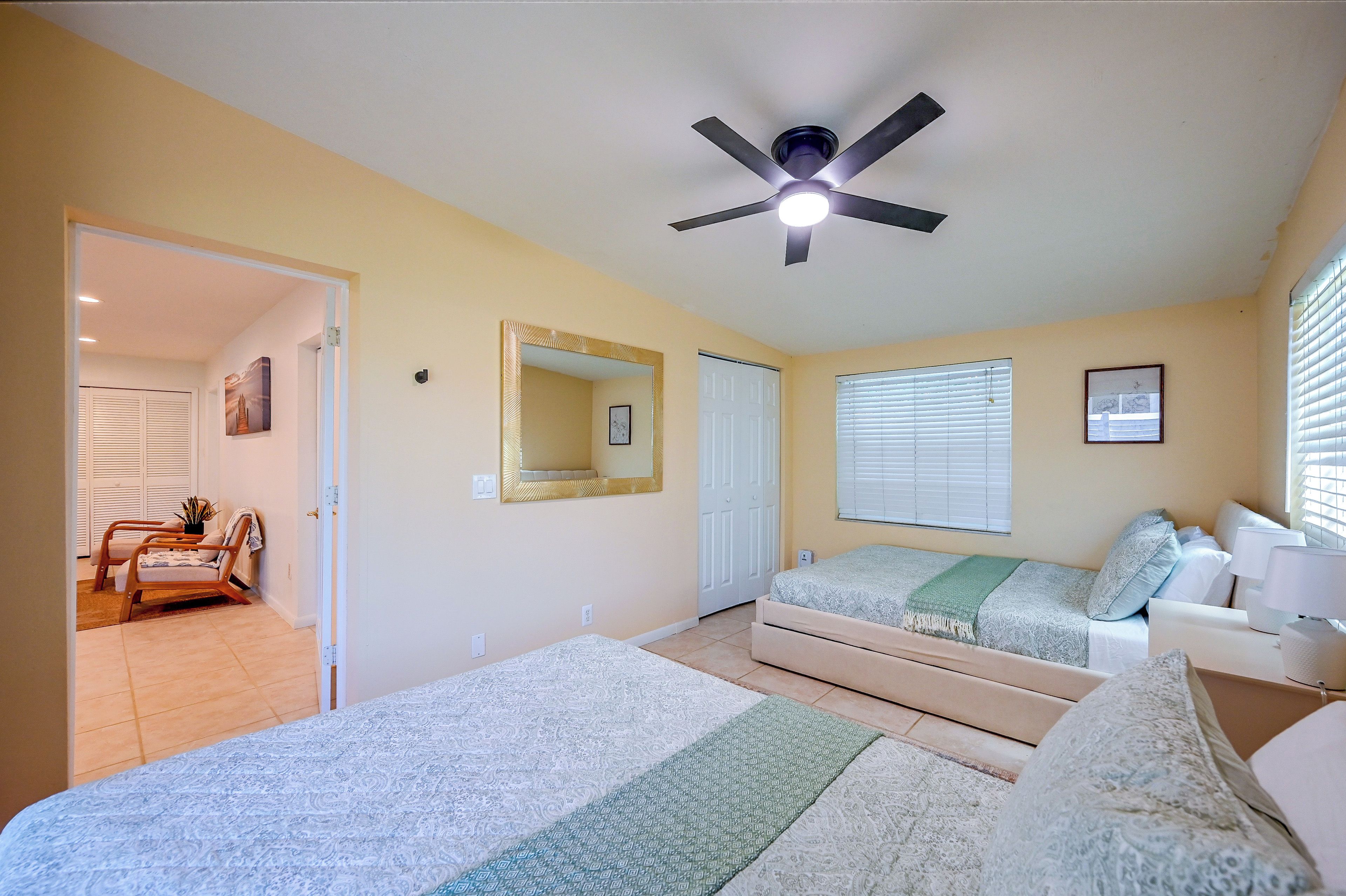 A bedroom with a bed, a ceiling fan, a window with blinds, and a door leading to another room.