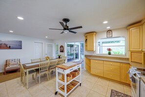 Une cuisine spacieuse avec des meubles en bois, un coin repas comprenant une table et des chaises, et un ventilateur de plafond.