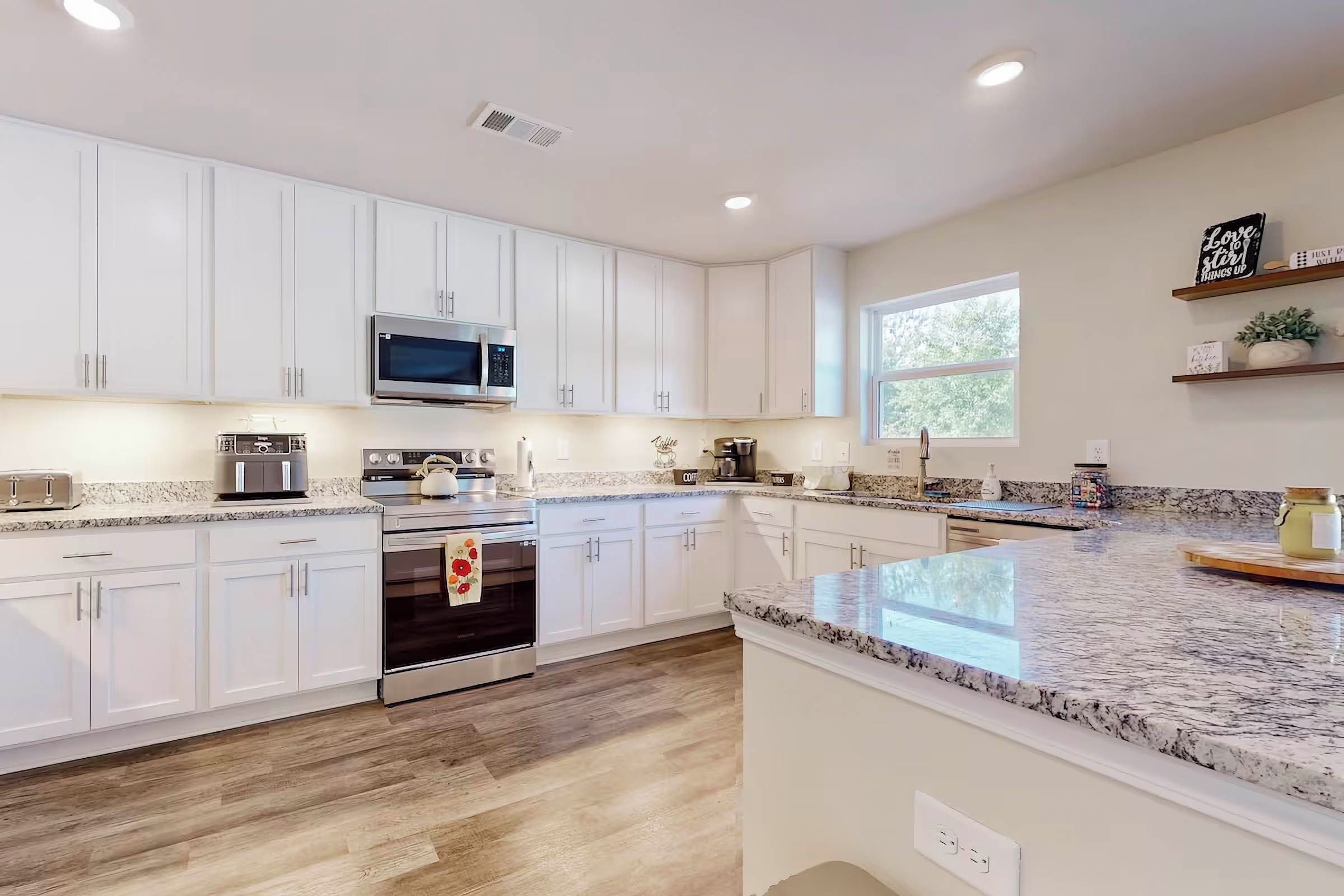 A modern kitchen with white cabinets, stainless steel appliances, a granite countertop, and a large window providing natural light.