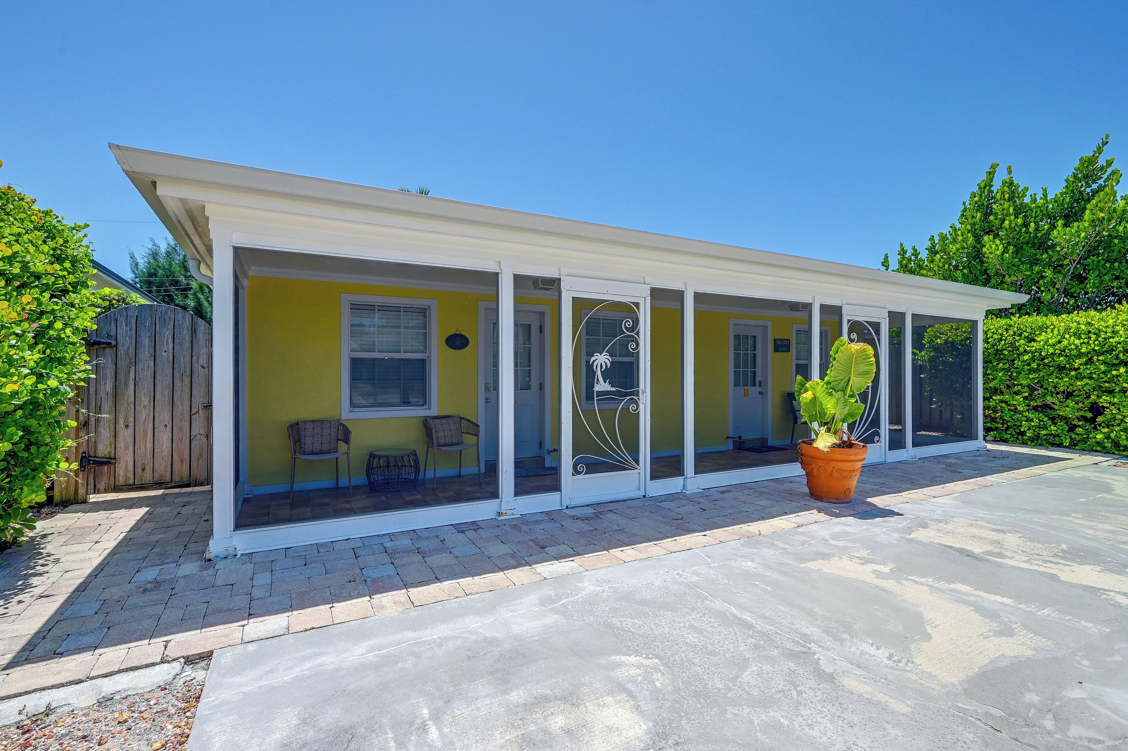 A covered patio area with a yellow wall, two windows, and a door.