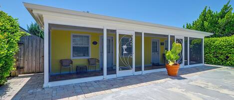 A covered patio area with a yellow wall, two windows, and a door.