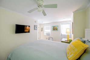 A bedroom with a bed, a television mounted on the wall, a ceiling fan, and a window with blinds. - Prime Naples Park Location! Beachy Duplex (Naples)