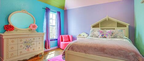 A bedroom with a bed, dresser, and a window with curtains.