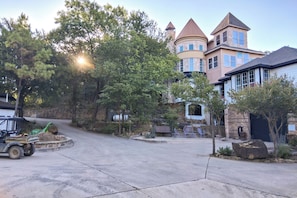 A residential area with a large house featuring a turret and stone walls, a paved driveway, and a forklift in the foreground.