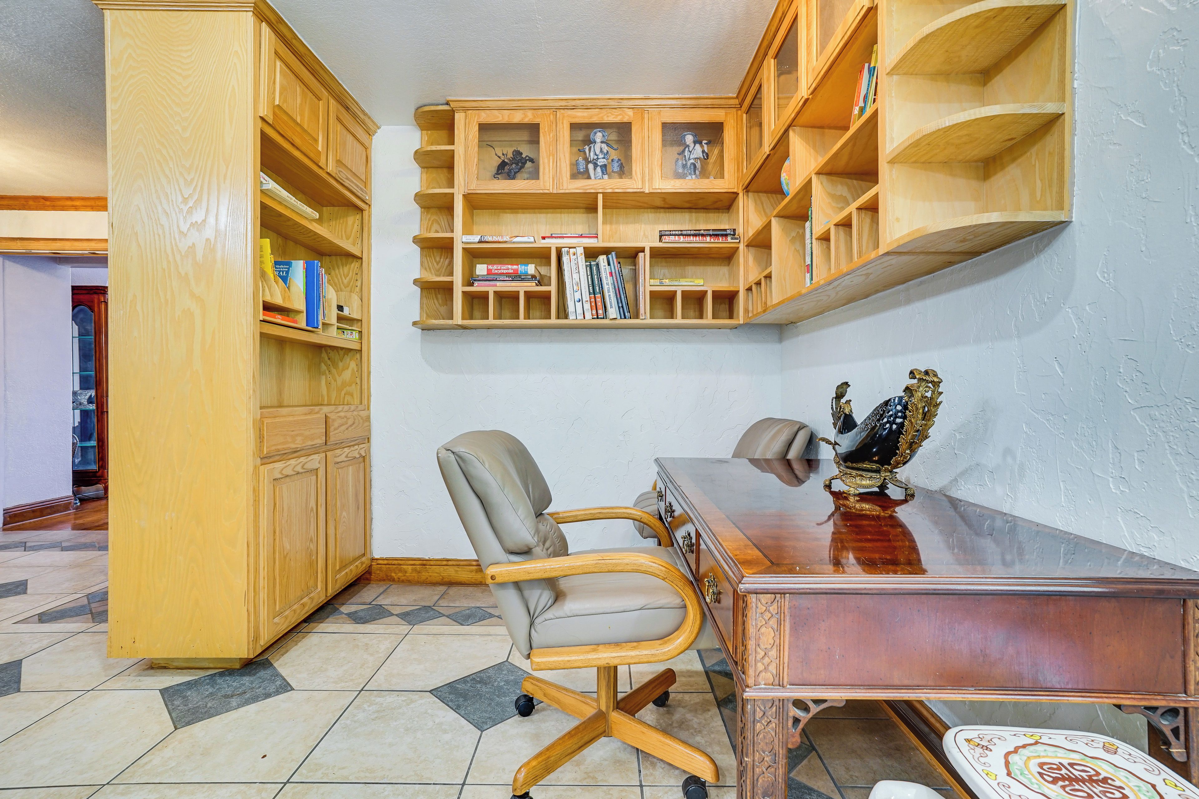Une pièce comprenant un bureau en bois, une chaise, une bibliothèque et un objet décoratif posé sur le bureau.