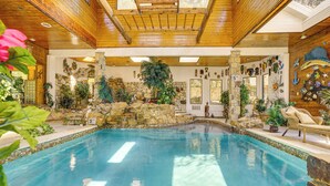 A large indoor swimming pool with a stone wall and waterfall feature, surrounded by various plants and decorative items. - Family Retreat Ready! 'castlewood Ranch' in Chico (Chico)