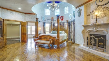 A spacious bedroom with a four-poster bed, a fireplace, and a chandelier.