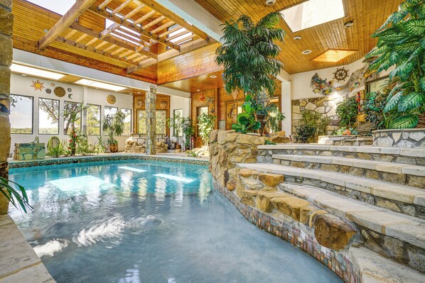 Une piscine avec des marches en pierre menant à une terrasse en bois, entourée de différentes plantes et d’éléments décoratifs.