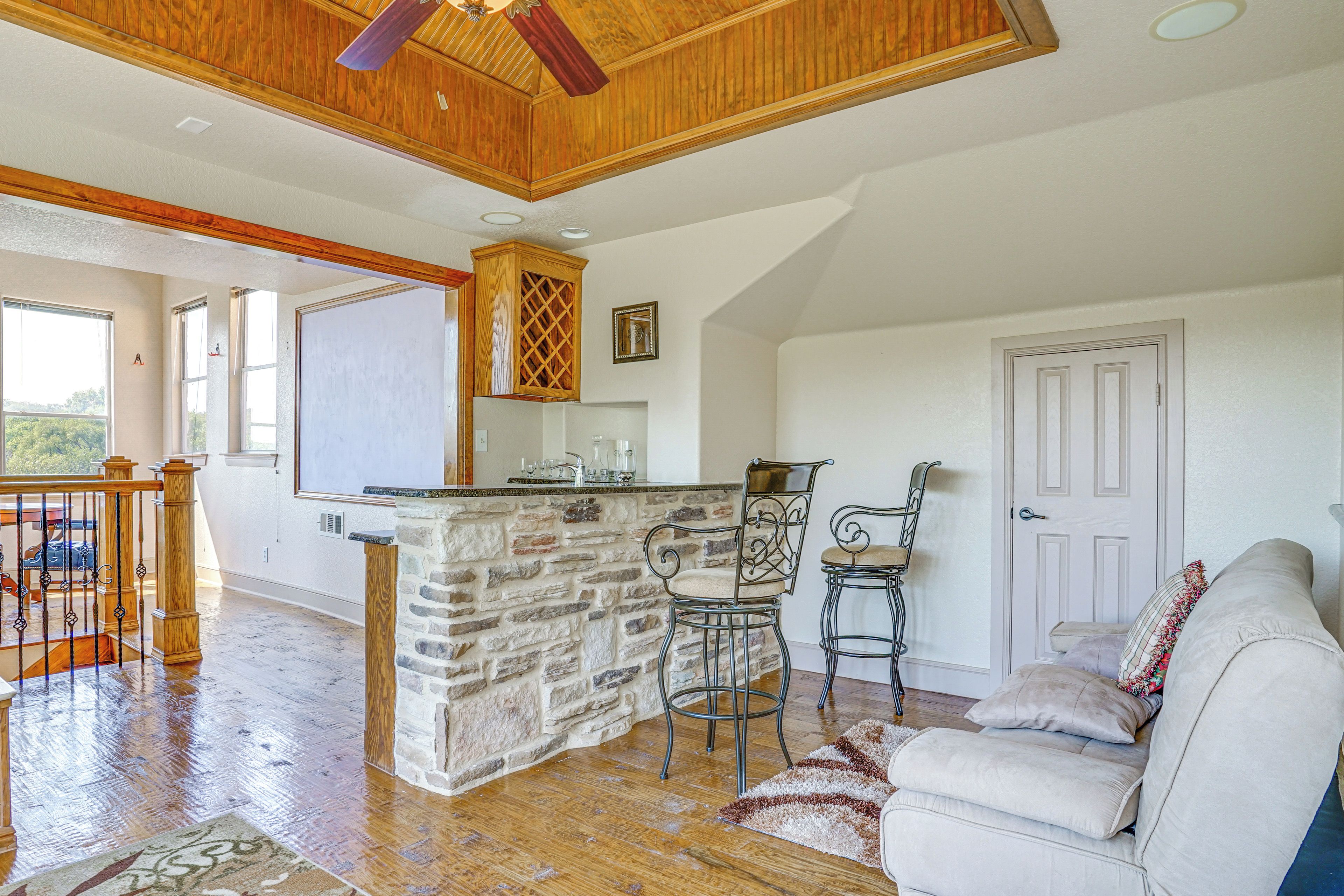 A spacious living area with a stone fireplace, wooden ceiling, and a large window.