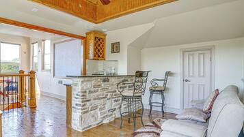 A spacious living area with a stone fireplace, wooden ceiling, and a large window.
