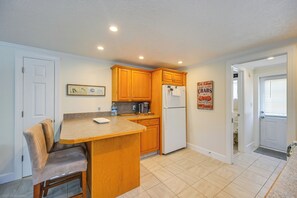 A compact kitchen with wooden cabinets, a built-in microwave, a refrigerator, and a small dining area with a chair. - 2 Mi to Beach! Naples Park Bungalow (Naples)