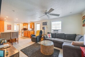 A spacious living area with a grey sofa, a dining table with chairs, a kitchen with wooden cabinets, and a ceiling fan. - 2 Mi to Beach! Naples Park Bungalow (Naples)