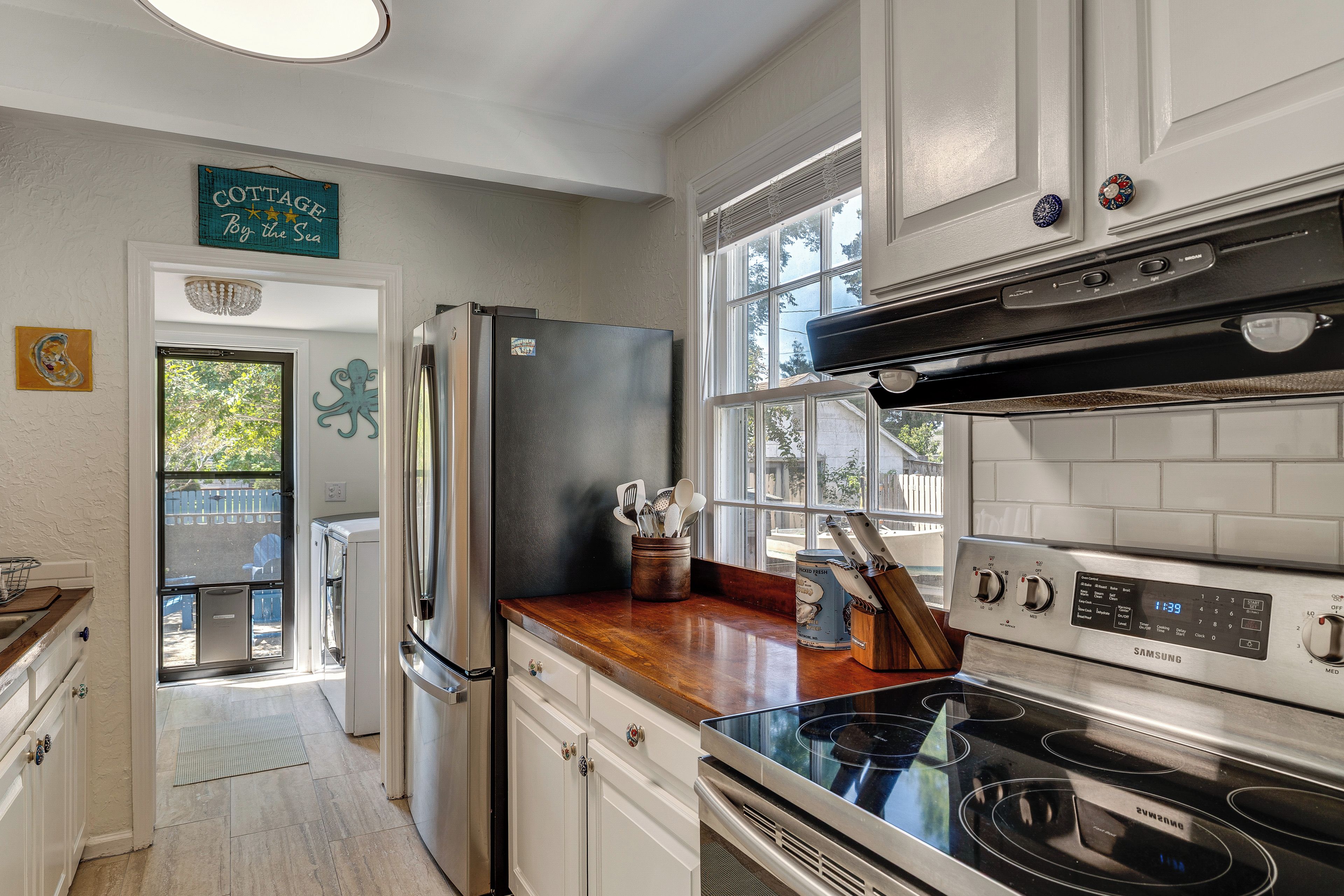 A kitchen with white cabinets, a stainless steel refrigerator, a black stove, and a window with a view of the outdoors.