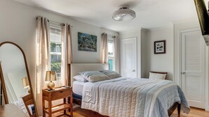 Et soveværelse med seng, et natbord, en lampe, et vindue med gardiner, en loftlampe og en dør.