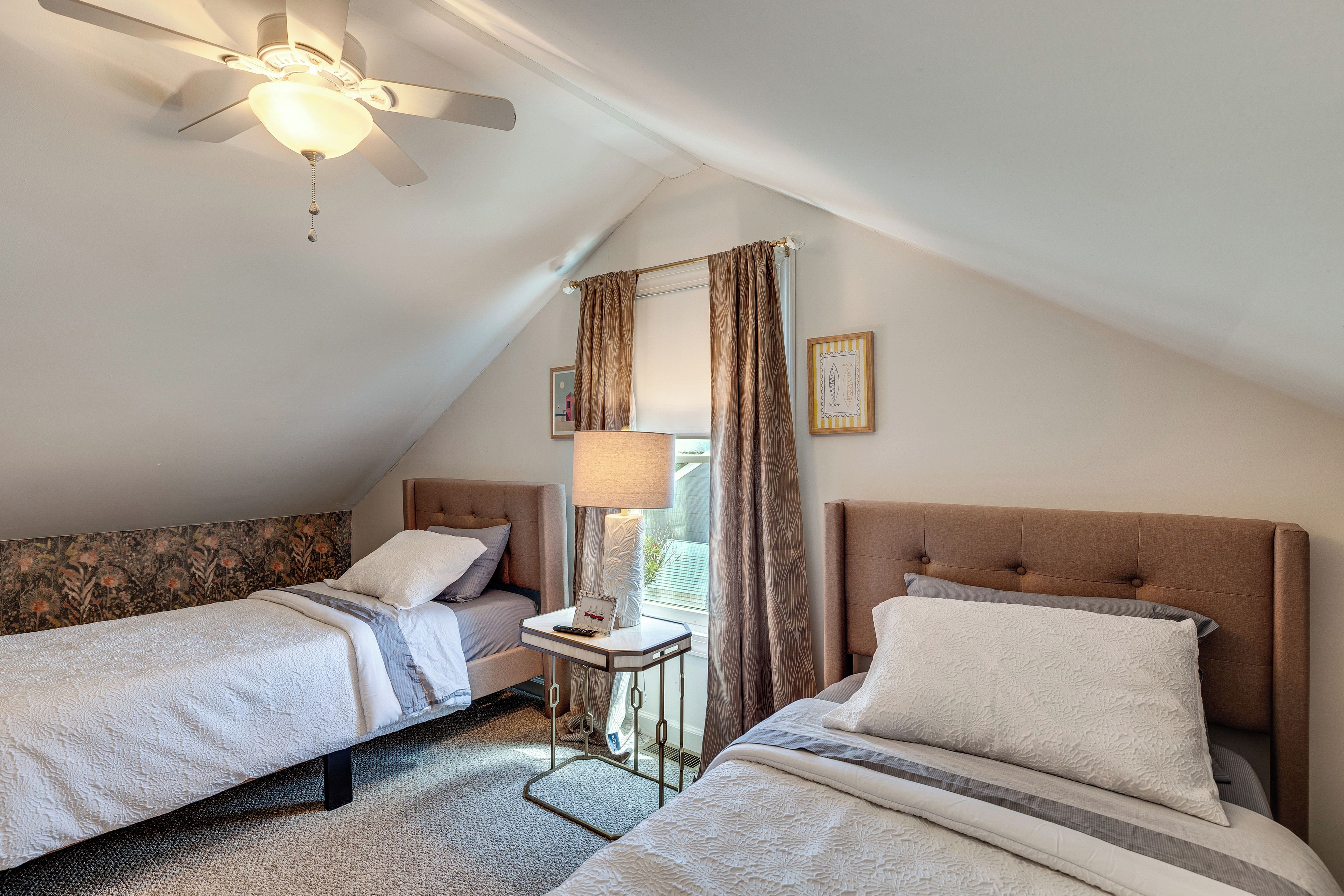 A bedroom with two beds, a ceiling fan, a nightstand, and a window with curtains.