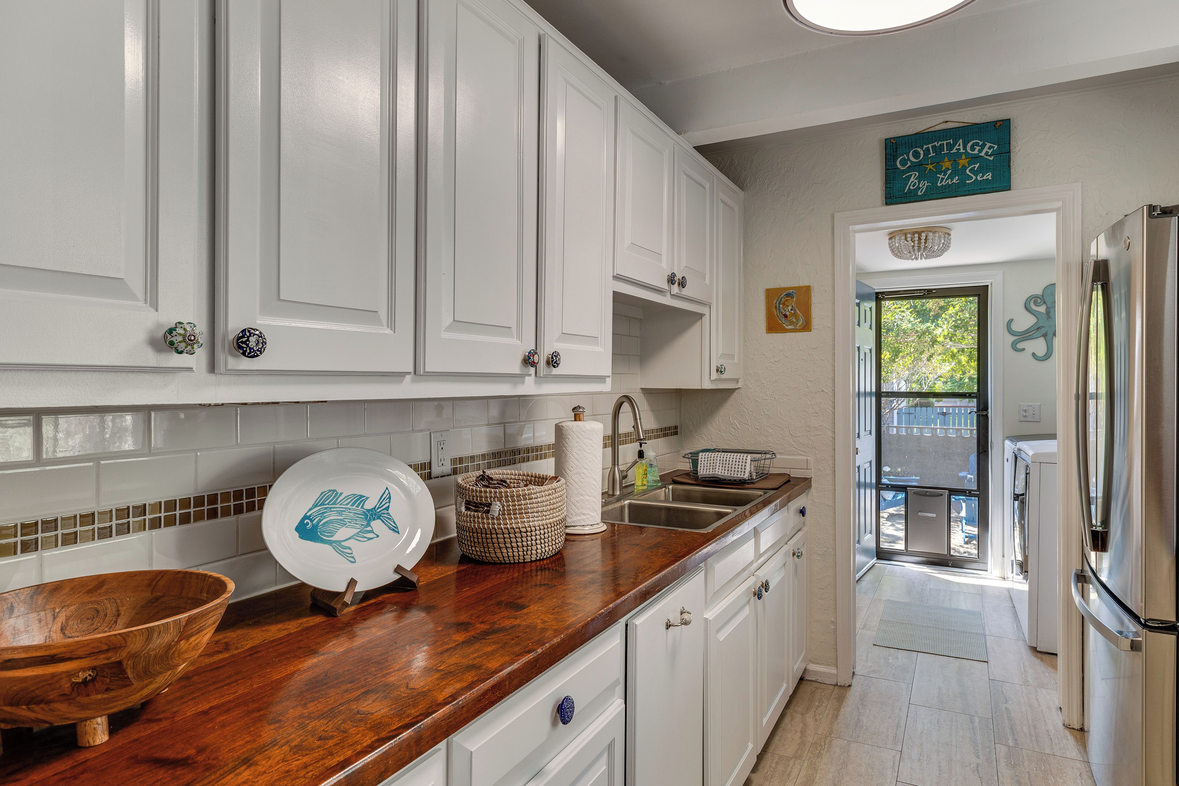 A kitchen with white cabinets, a wooden countertop, a sink, and a stainless steel refrigerator.