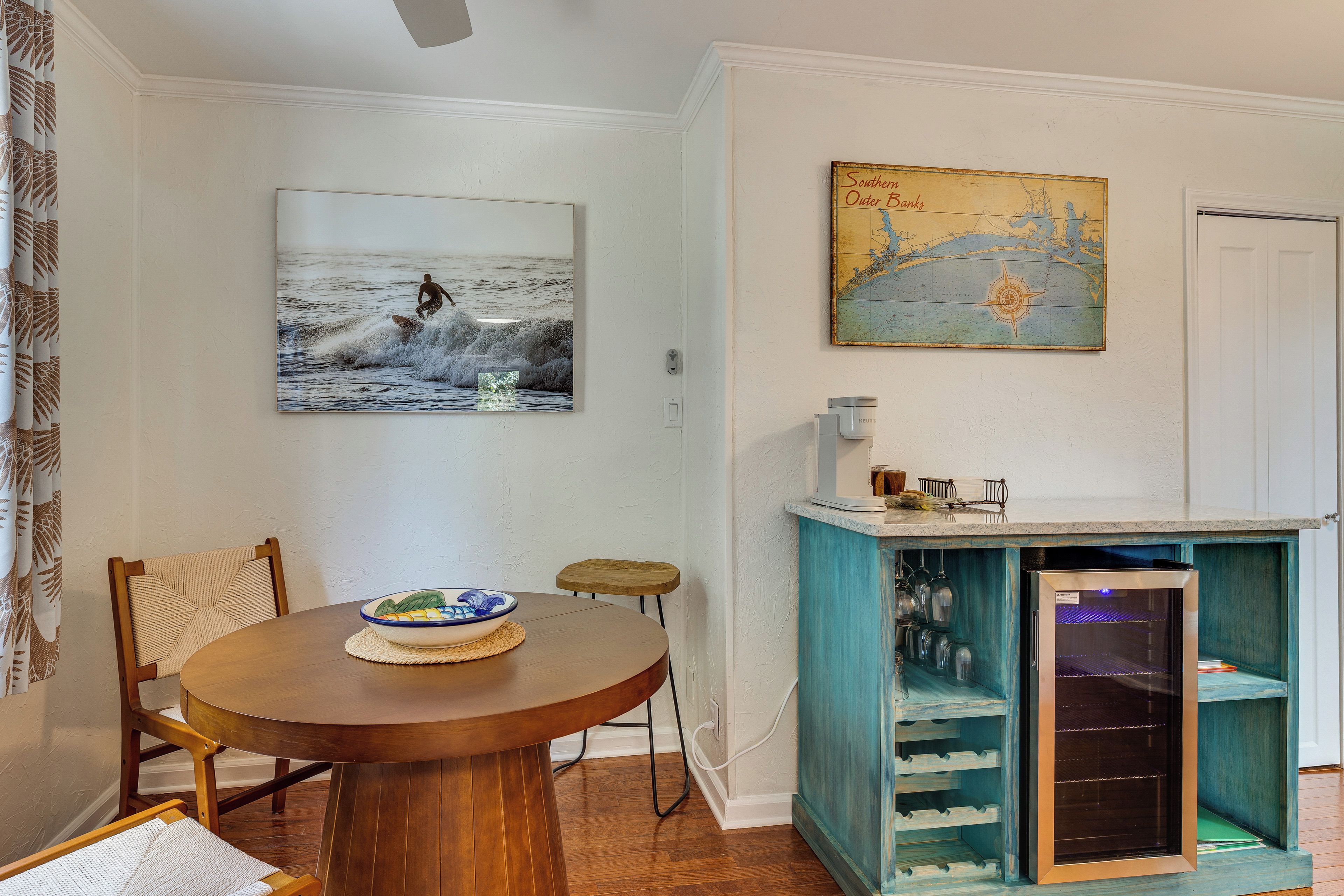 Un coin repas avec une table en bois, des chaises, un bol et un tableau accroché au mur.