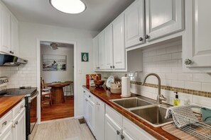 A kitchen with white cabinets, a wooden countertop, a stainless steel sink, and a dining area with a wooden table and chairs.