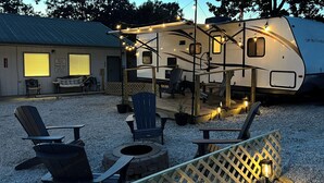 Een camper met een overdekte veranda, buitenzitplaatsen met Adirondack-stoelen, en een grindpad.