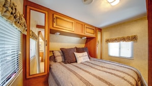 Een slaapkamer met een bed, een raam met zonwering, een deur en houten kastjes.