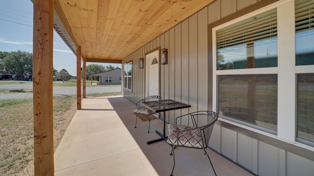 A covered patio area with a table and chairs, a door, and a window with blinds. - Gateway to State Park & Lake! Inviting Vian Cabin (Gore)