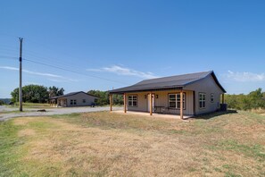 A single-story building with a covered porch and a large window, surrounded by a grassy area and a gravel path.