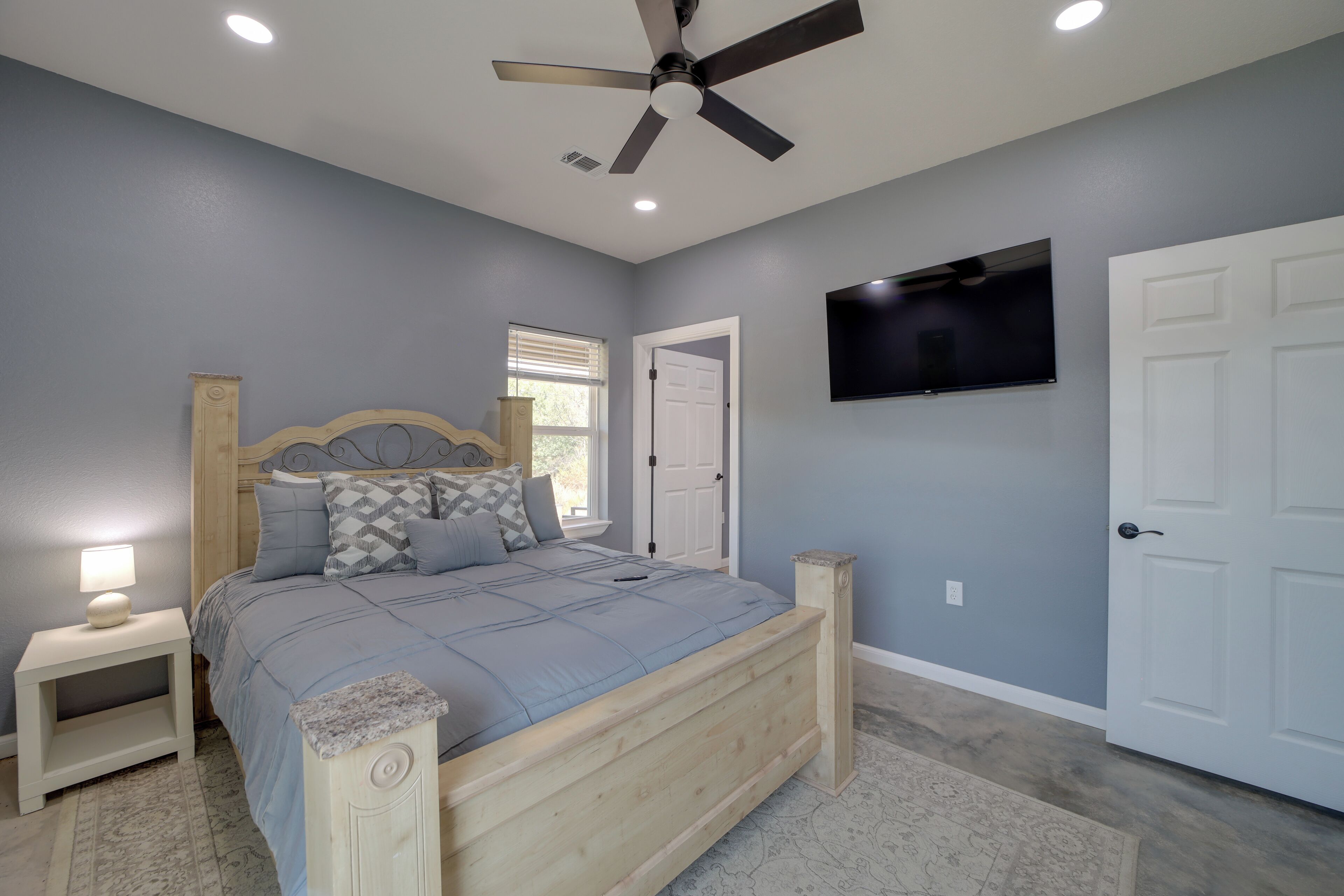A bedroom with a bed, nightstand, ceiling fan, TV, and a door.