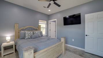 A bedroom with a bed, nightstand, ceiling fan, TV, and a door.
