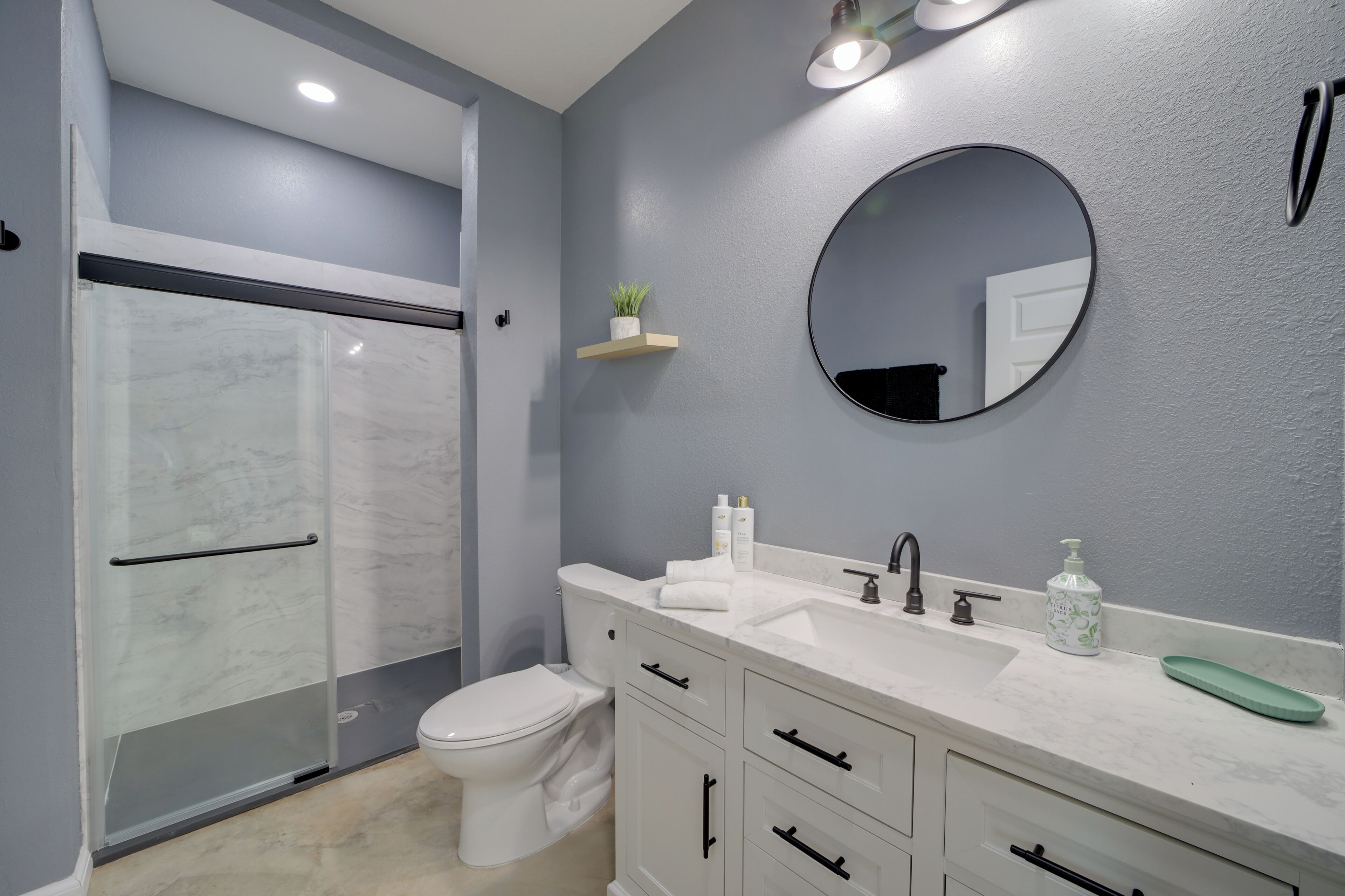A modern bathroom with a glass shower enclosure, a toilet, a sink with a mirror, and a vanity with drawers.