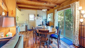 A cozy cabin interior with a wooden dining table, chairs, a sofa, and a kitchen area.
