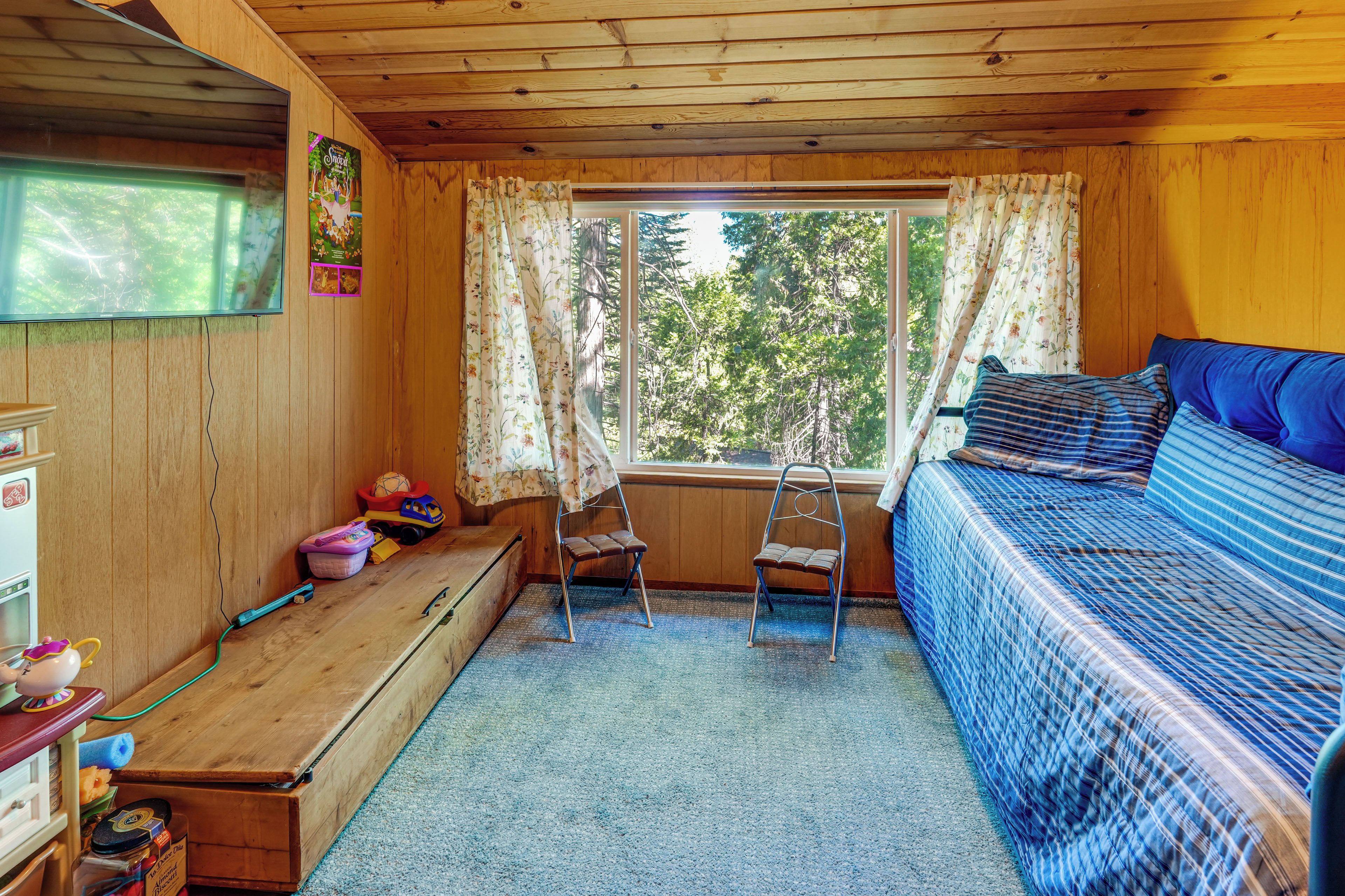 Quarto aconchegante com cama, janela com cortinas, uma mesinha e uma escada.
