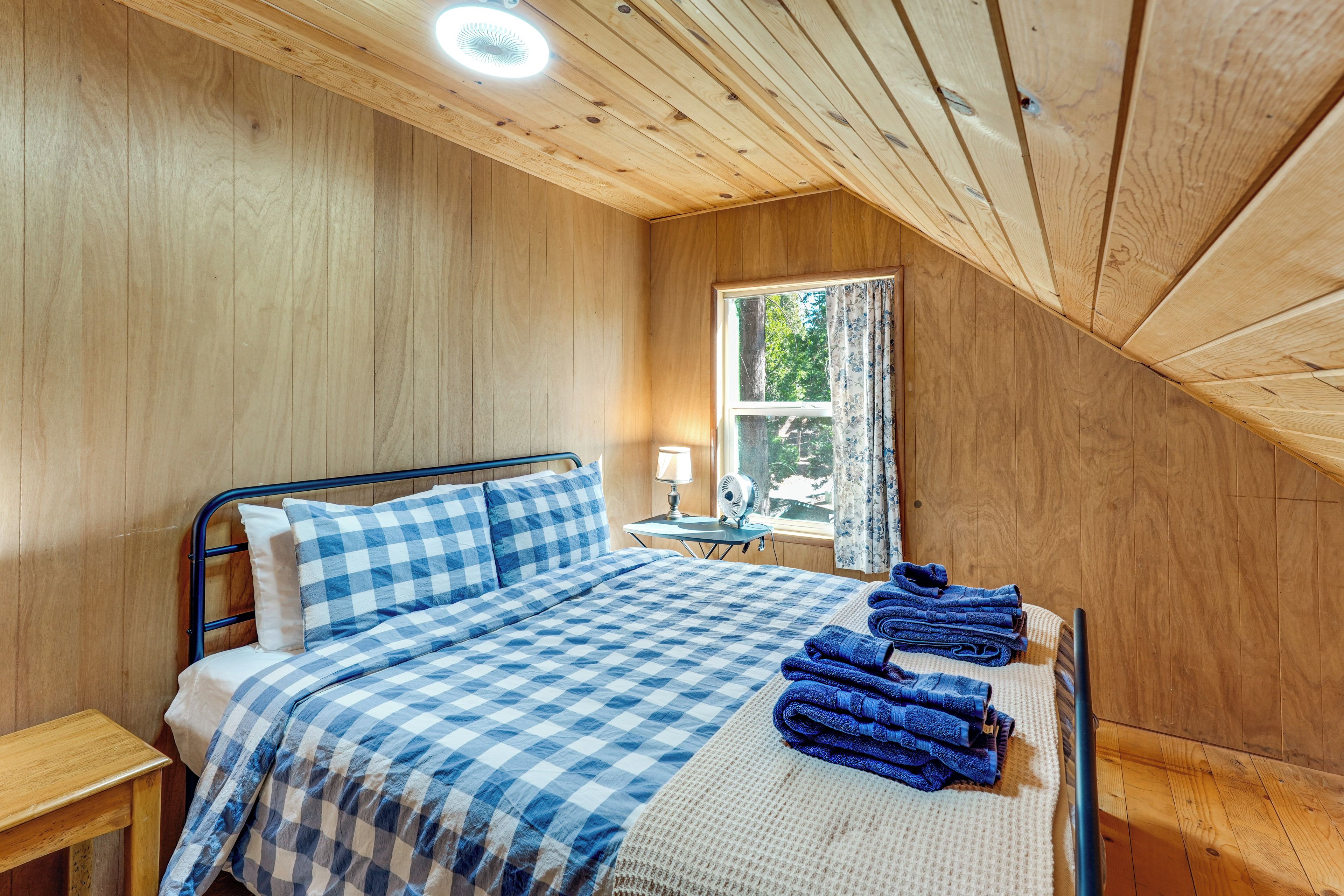 A bedroom with a bed, a nightstand, a window with curtains, and a ceiling fan.
