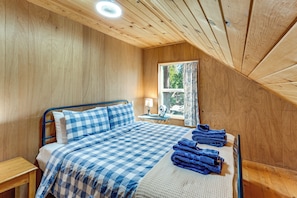 A bedroom with a bed, a nightstand, a window with curtains, and a ceiling fan.