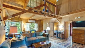 A spacious living area with a high ceiling, wooden beams, a sofa, a coffee table, and a television.